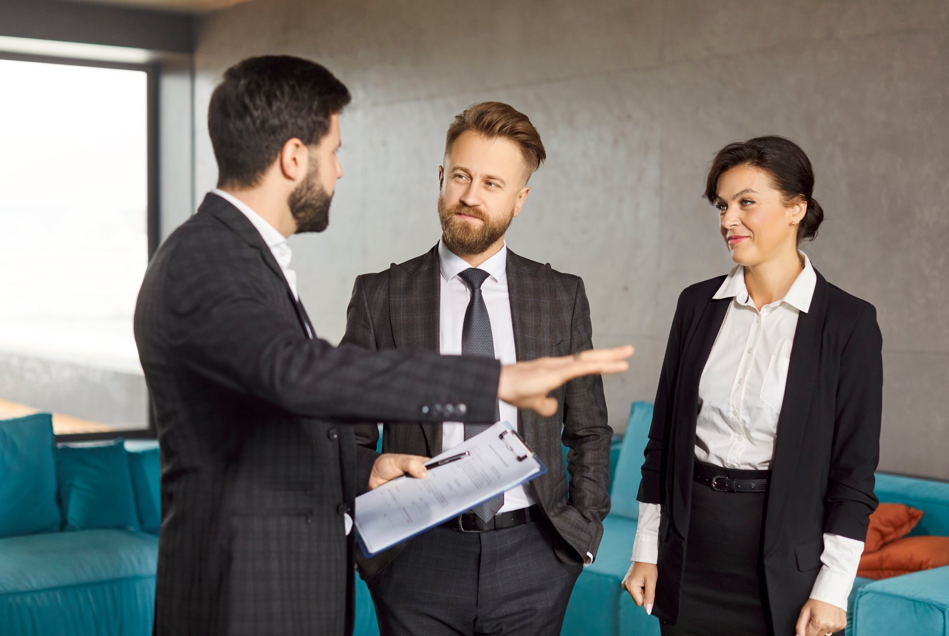 Three people standing in a room with green couches and one person holding a clipboard