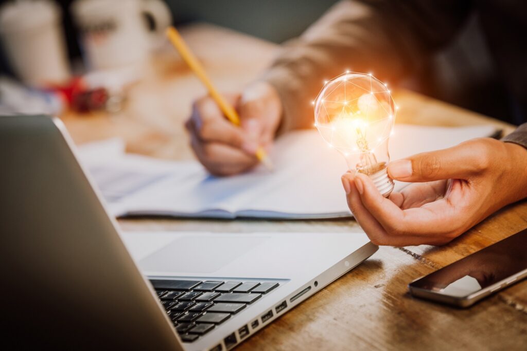 A person holds a light bulb above a laptop | Wallach & Associates, P.C.
