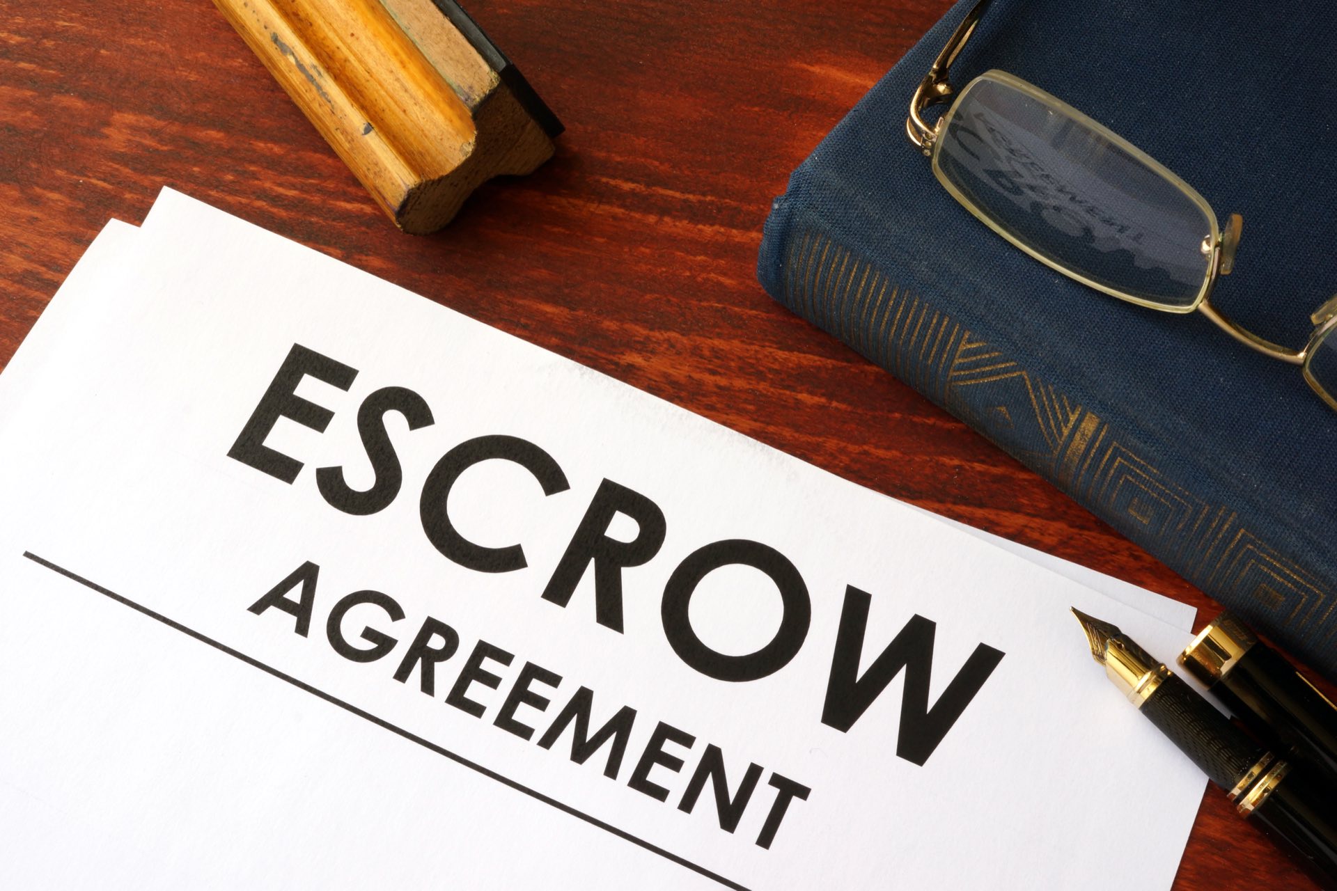 Paper that reads Escrow Agreement next to a book and glasses