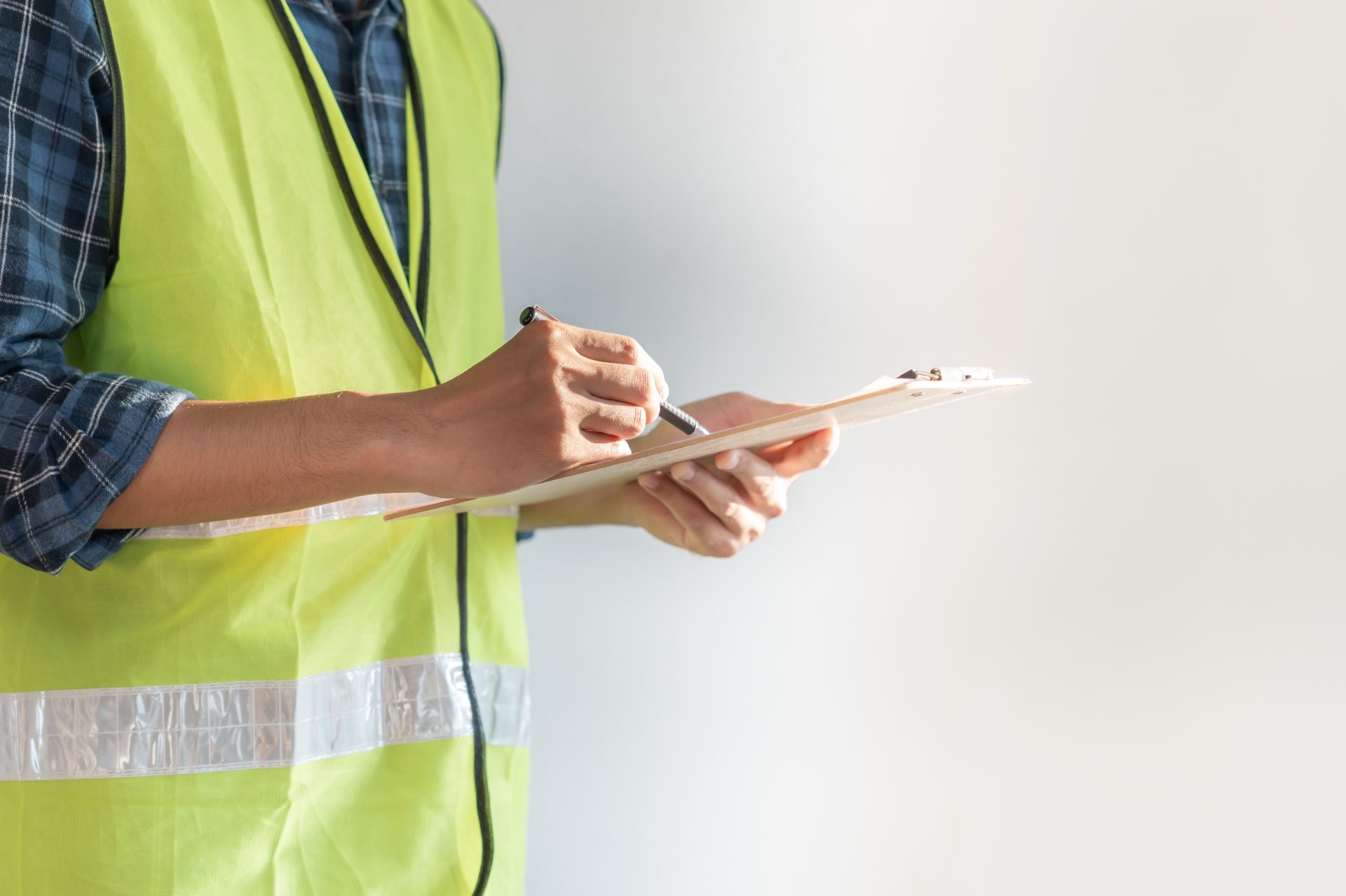 Person holding a pencil and clipboard in a yellow vest
