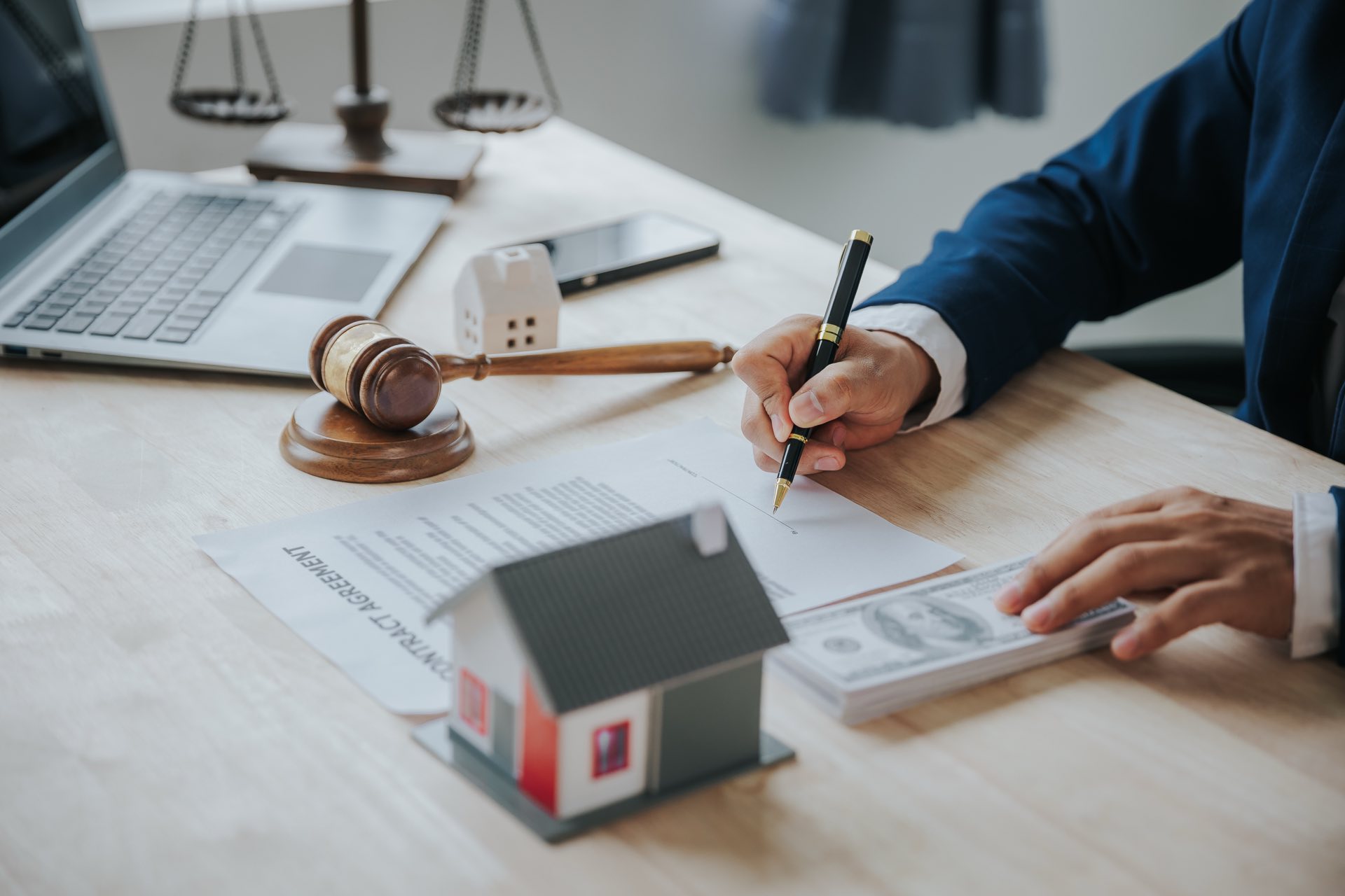 Person sitting at a desk with paperwork next to a gavel and small wooden house