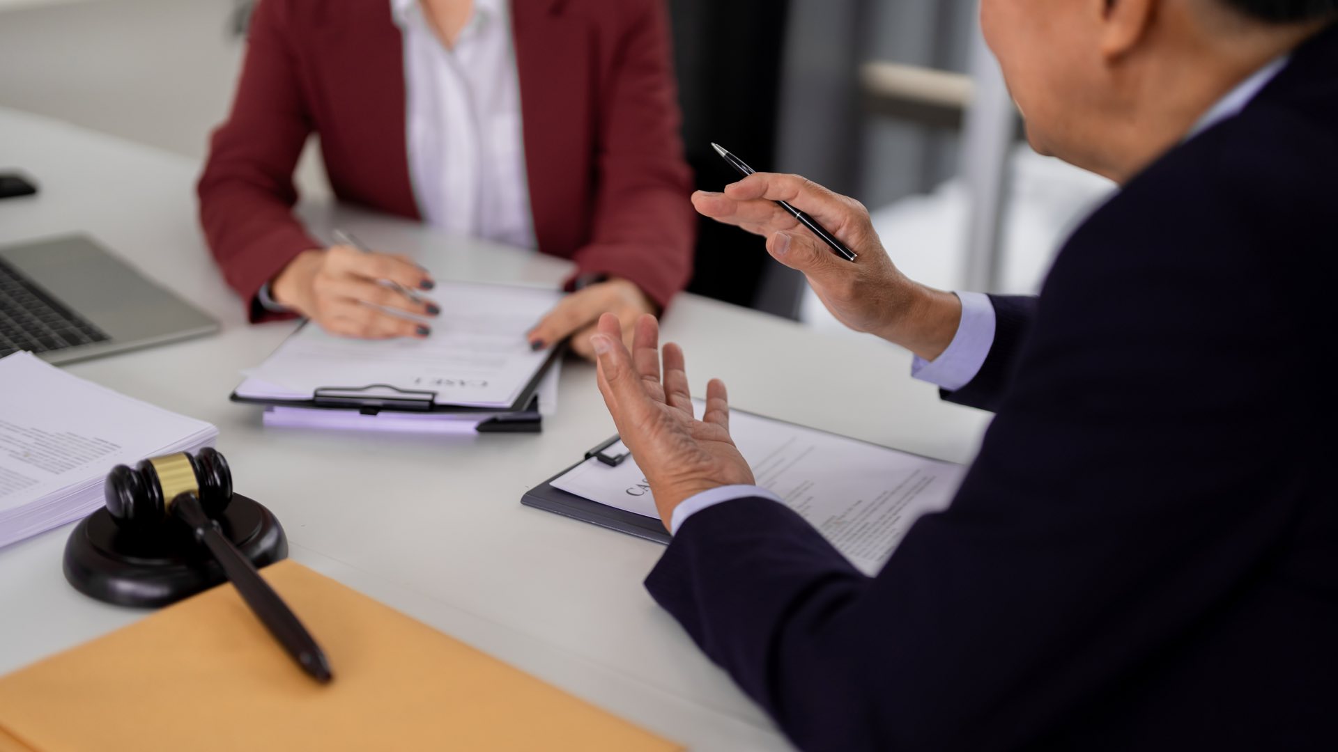 Zoomed in photo of two people sitting at a desk with pens in their hand and clipboards
